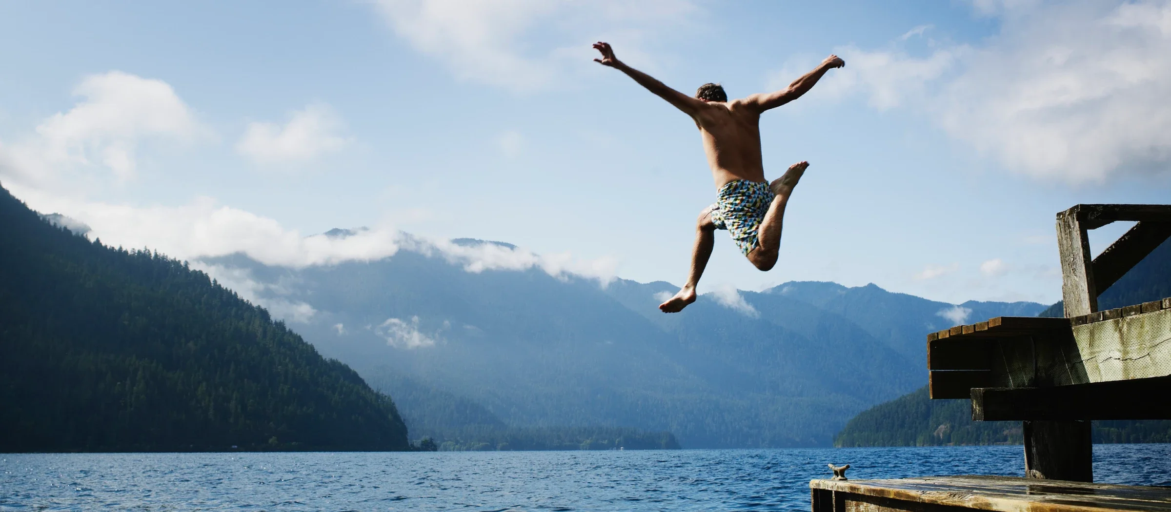 Mann springt von einem Steg in einen See. 