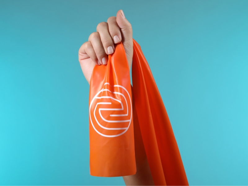 Oranges Theraband mit ENTDECKE DEIN NEO-Logo wird mit den Fingern festgehalten.