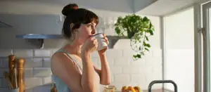 Frau trinkt aus Tasse in ihrer Küche.
