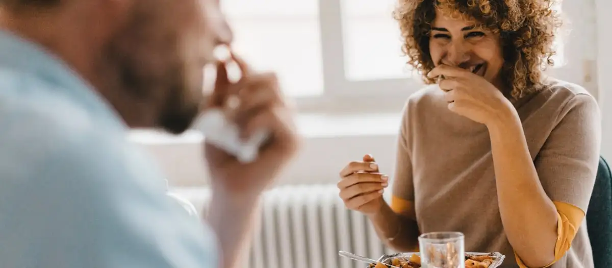 Frau und Mann sitzen am Tisch und essen und lachen dabei.