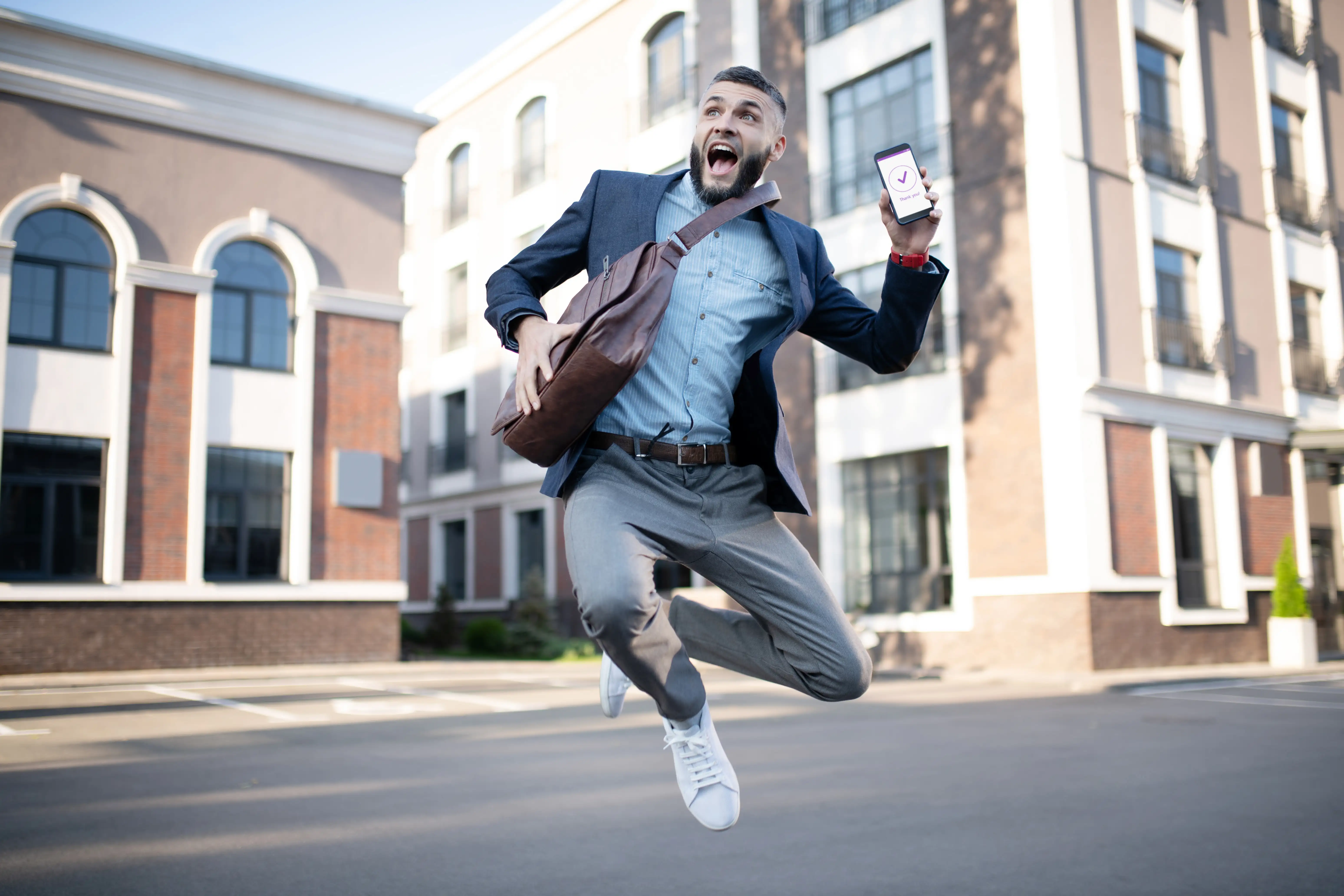 Mann springt in die Luft und hält sein Mobiltelefon in der Hand.