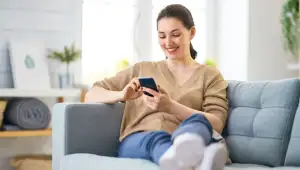 Frau sitzt entspannt auf dem Sofa und benutzt ihr Smartphone.