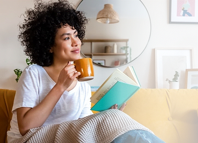Frau sitzt auf dem Sofa und hält eine Tasse in der Hand.