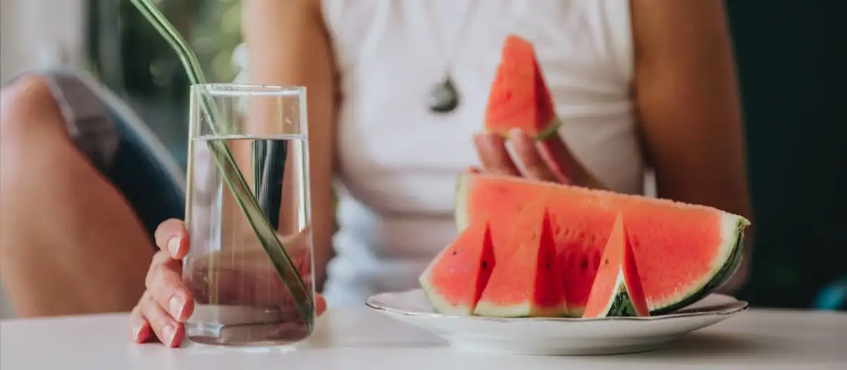 Frau mit Wasserglas und einem Stück Melone in der Hand