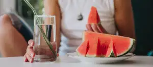 Frau mit Wasserglas und einem Stück Melone in der Hand