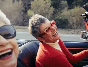 Zwei ältere Frauen mit Sonnenbrille sitzen im Cabrio und lachen.