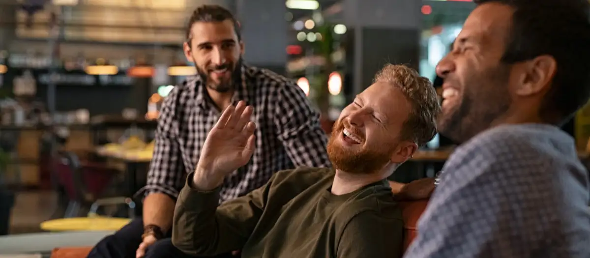 Drei Männer sitzen zusammen und lachen.