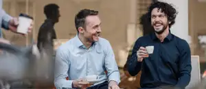 Männer sitzen draußen und trinken aus einer Tasse.