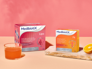 Medibiotix Lipo und Medibiotix Fit Packung neben Glas und Orange auf Steinplatte.