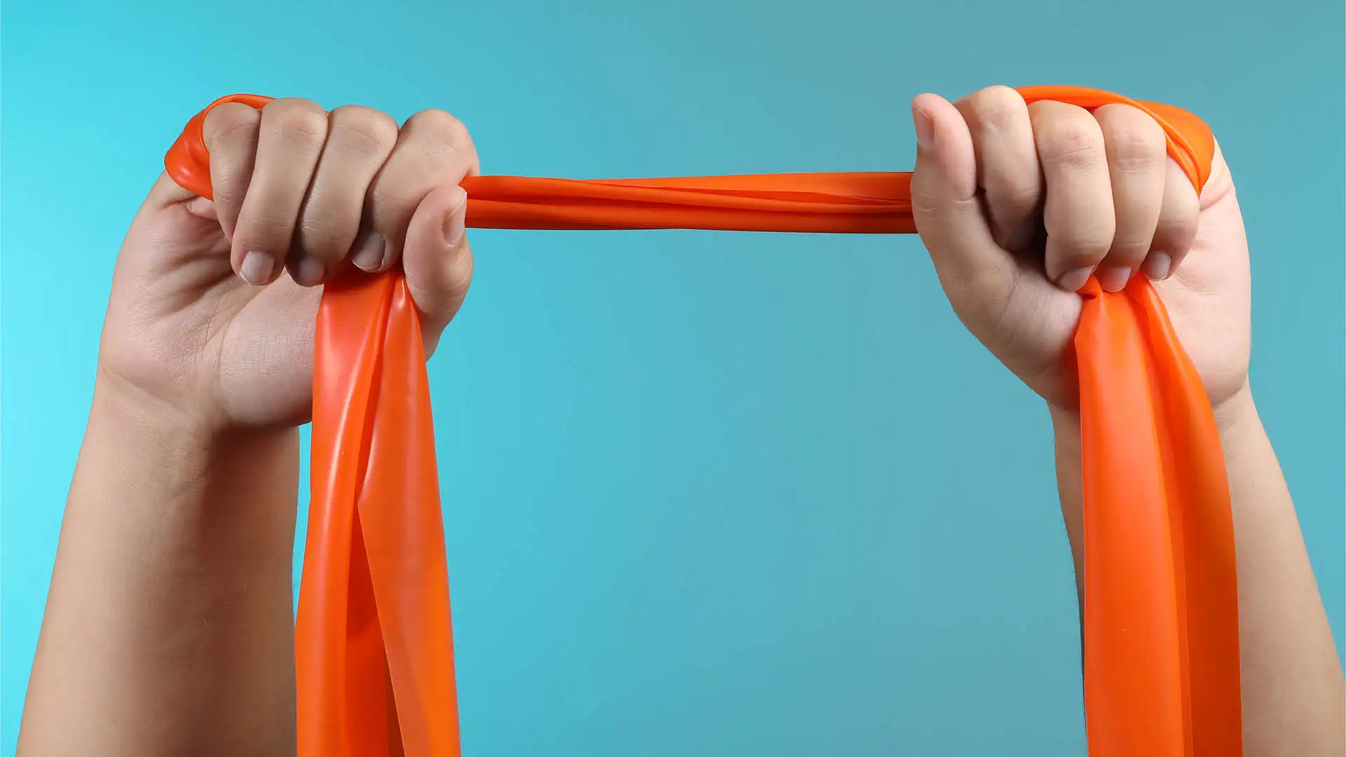 Oranges Theraband wird mit zwei Händen straffgezogen.