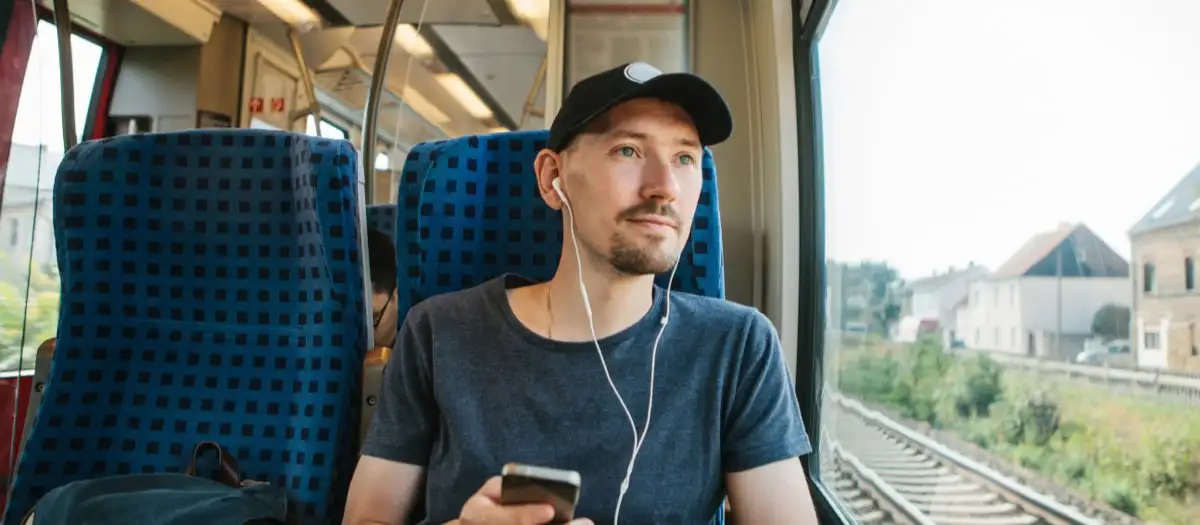 Mann sitzt im Zug und hört Musik.