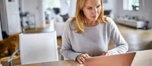 Frau sitzt an einem Tisch und arbeitet an einem Laptop.