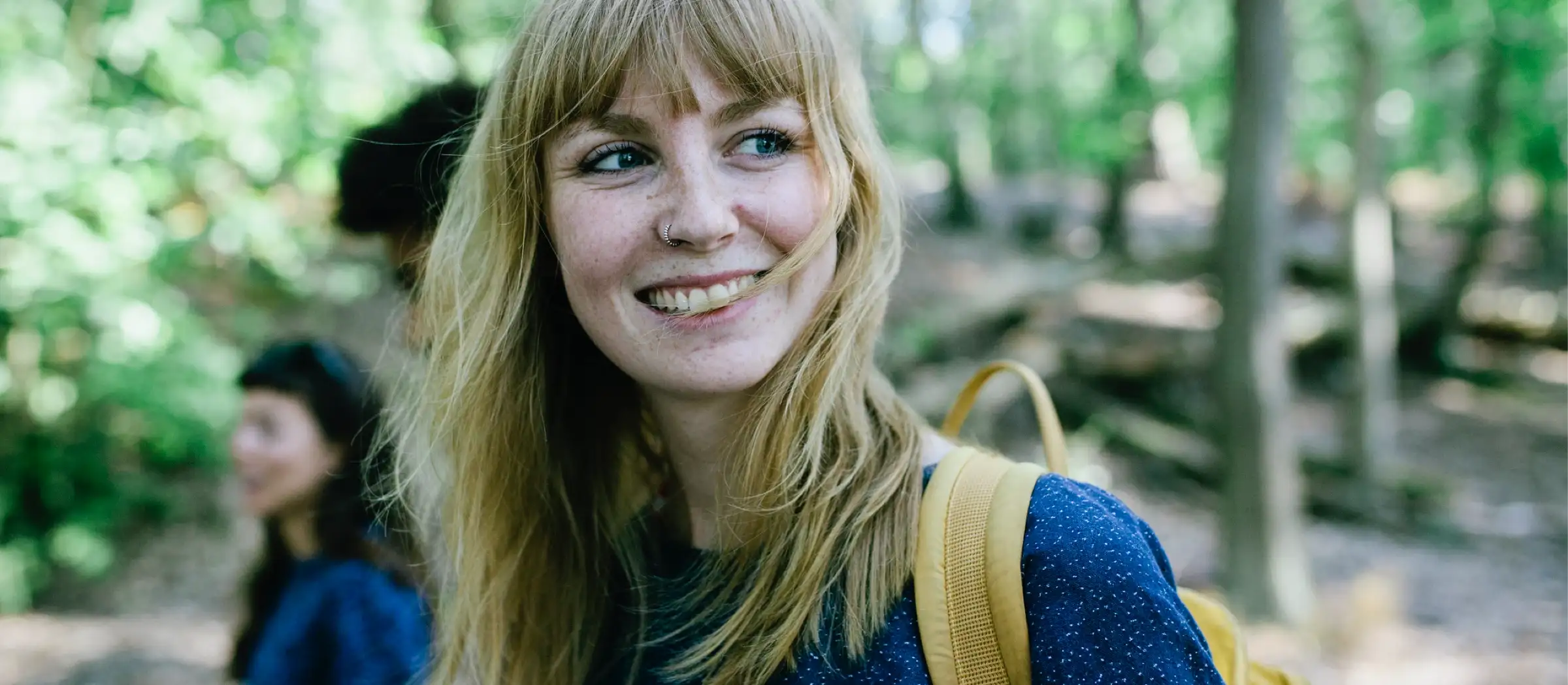 Frau steht im Wald und lacht.