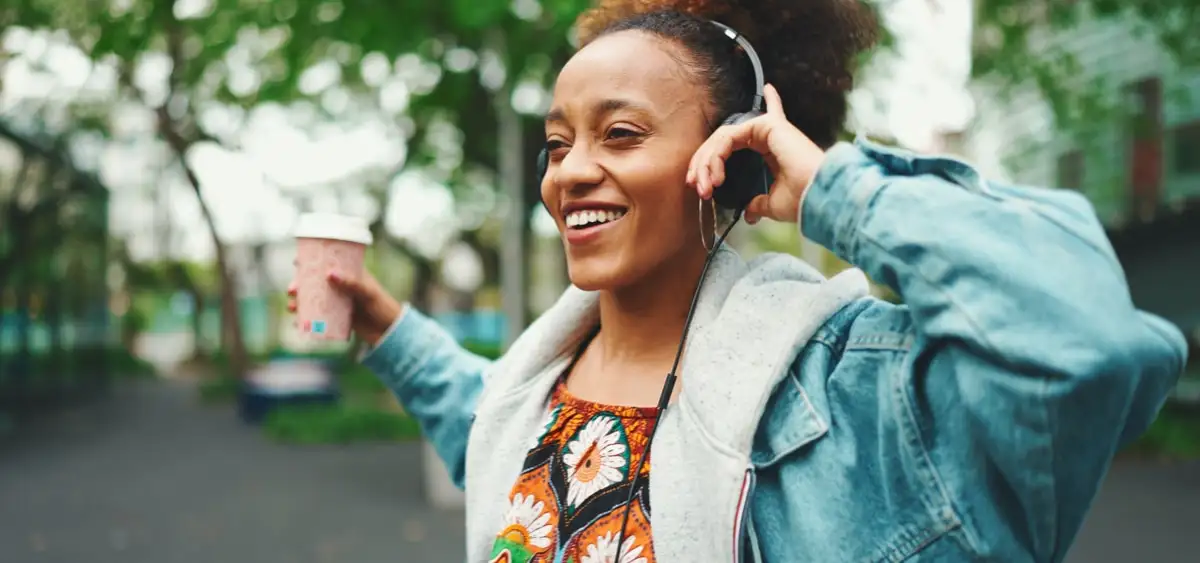 Frau startet mit Kaffee und Musik motiviert in den Tag, sie trägt Kopfhörer und hört Musik.