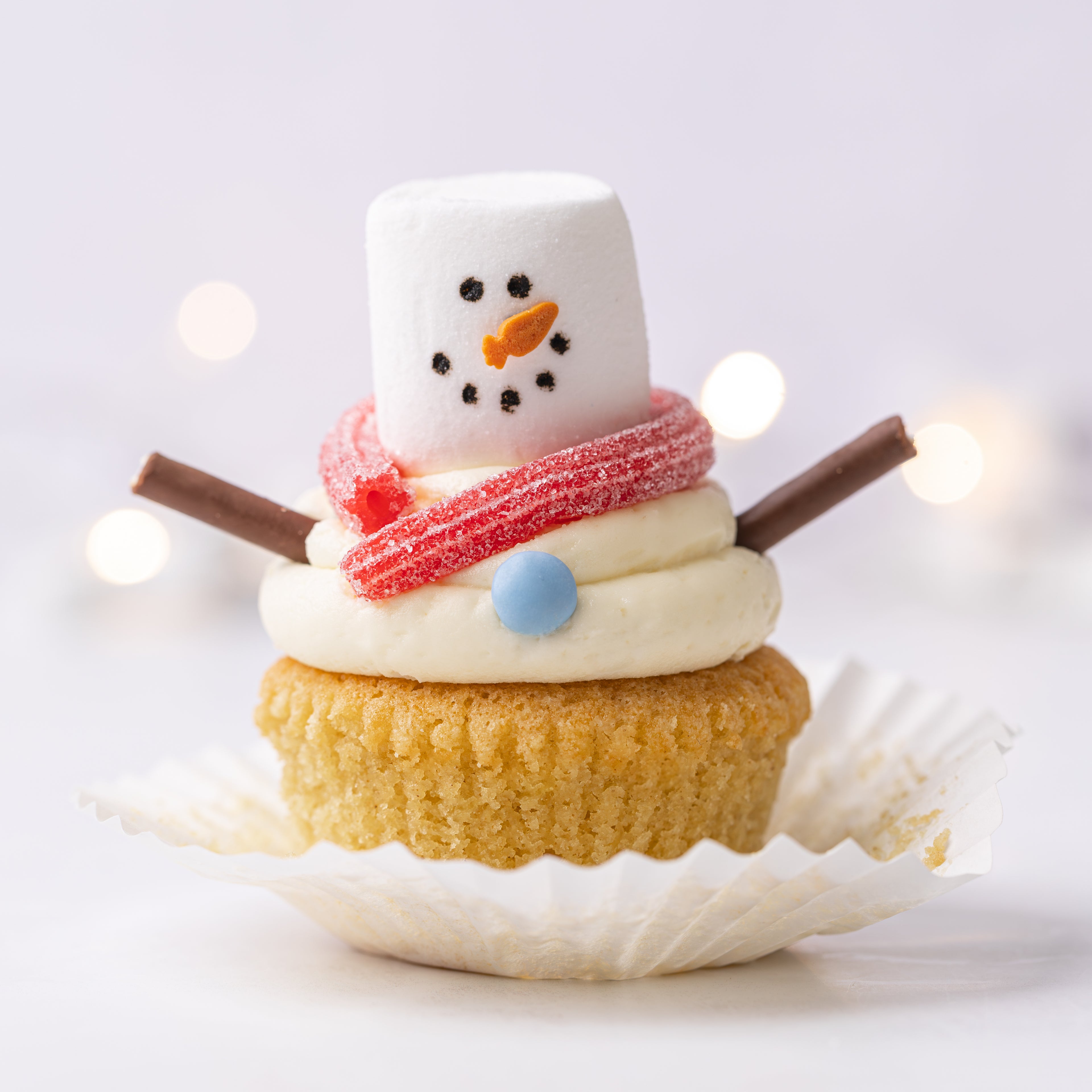 Vanilla cupcake decorated to replicate a snowman with edible sweets such as a marshmallow for a head.