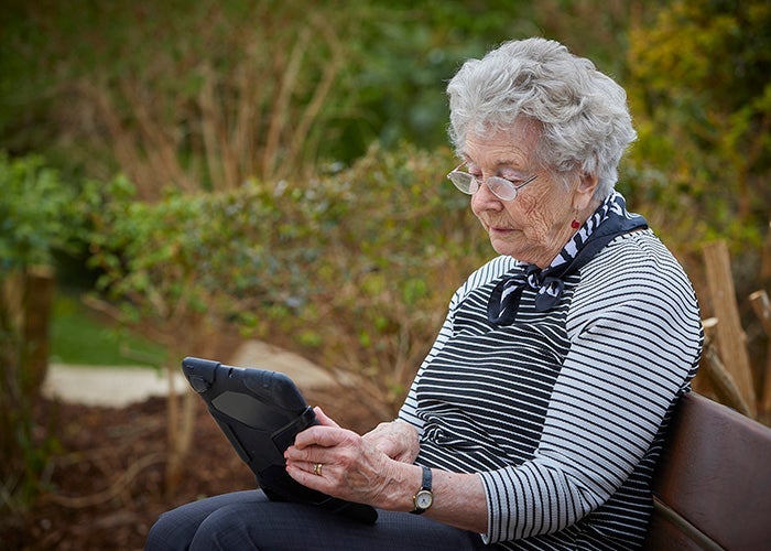 Elderly lady using her iPad to browse MySovereign, whilst sitting on an uncomfortable park bench