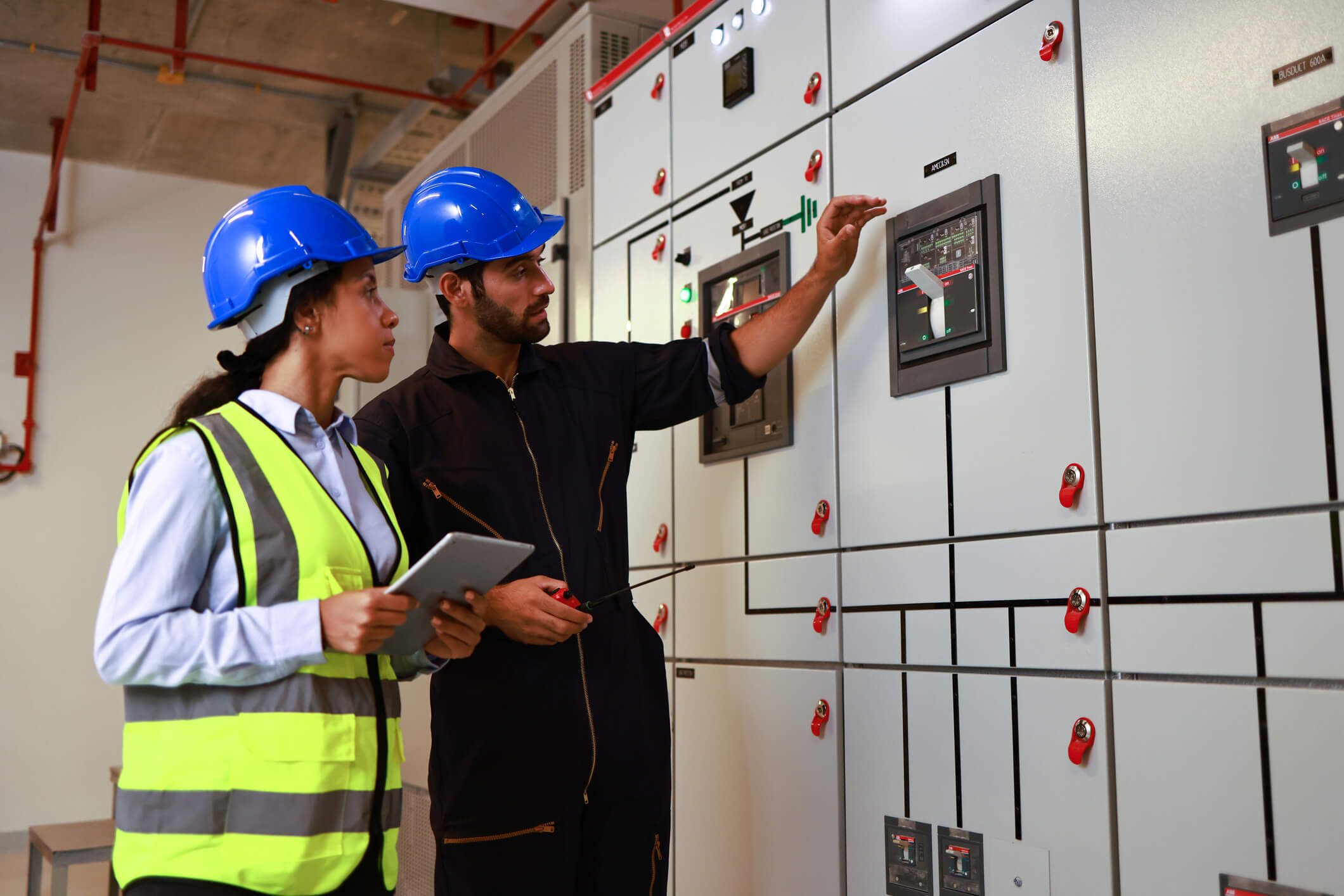 Male and Female colleague electrical engineer work checking at Electrical Distribution Control Room. The male workers hand hovers over an energy switch