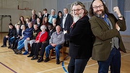 Dave Myers and Si King posing in a school hall, with programme contributors in the background.