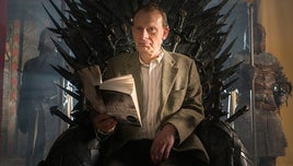 Presenter Andrew Marr sitting on a realisation of the Iron Throne from the Game of Thrones TV series. He is holding an open copy of a book that inspired the series, written by George RR Martin.