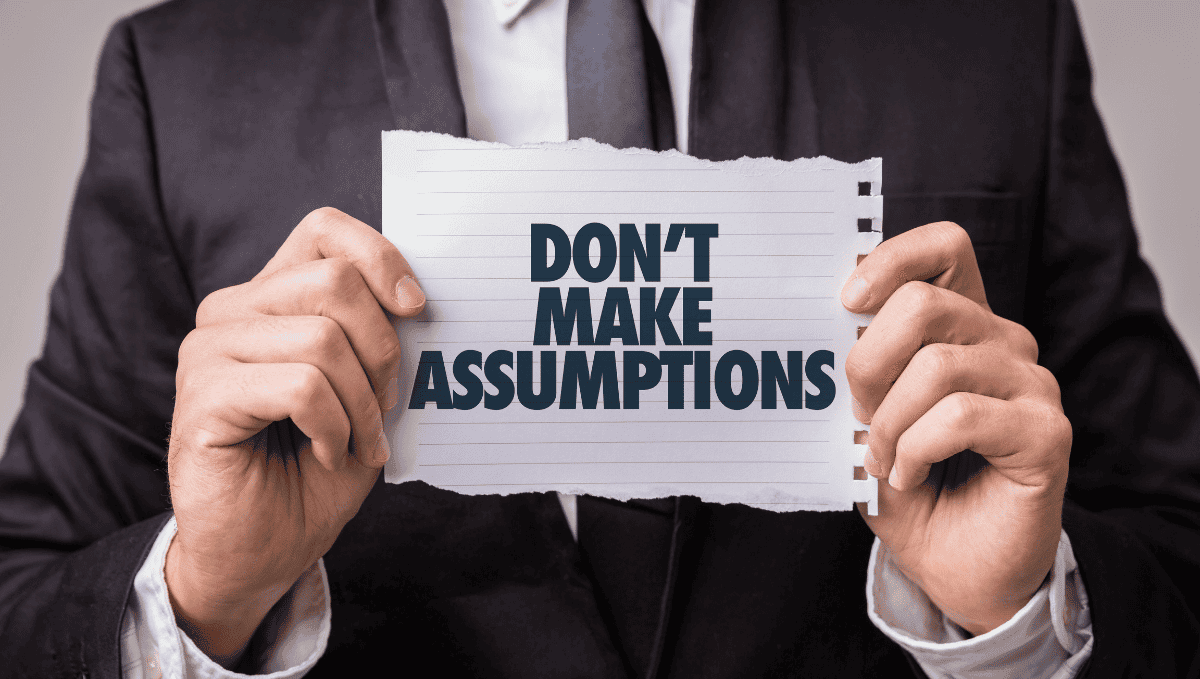 Man in suit holding a sign saying 'Don't make assumptions'