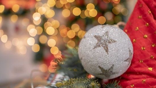 A glittery white bauble with golden stars against Christmas greenery red and gold material and a background of golden lights