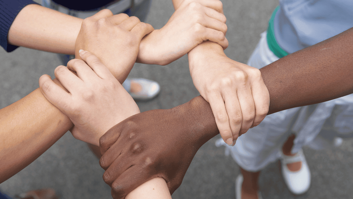 Five arms with different skin tones with hands locked on wrists representing racial equality.