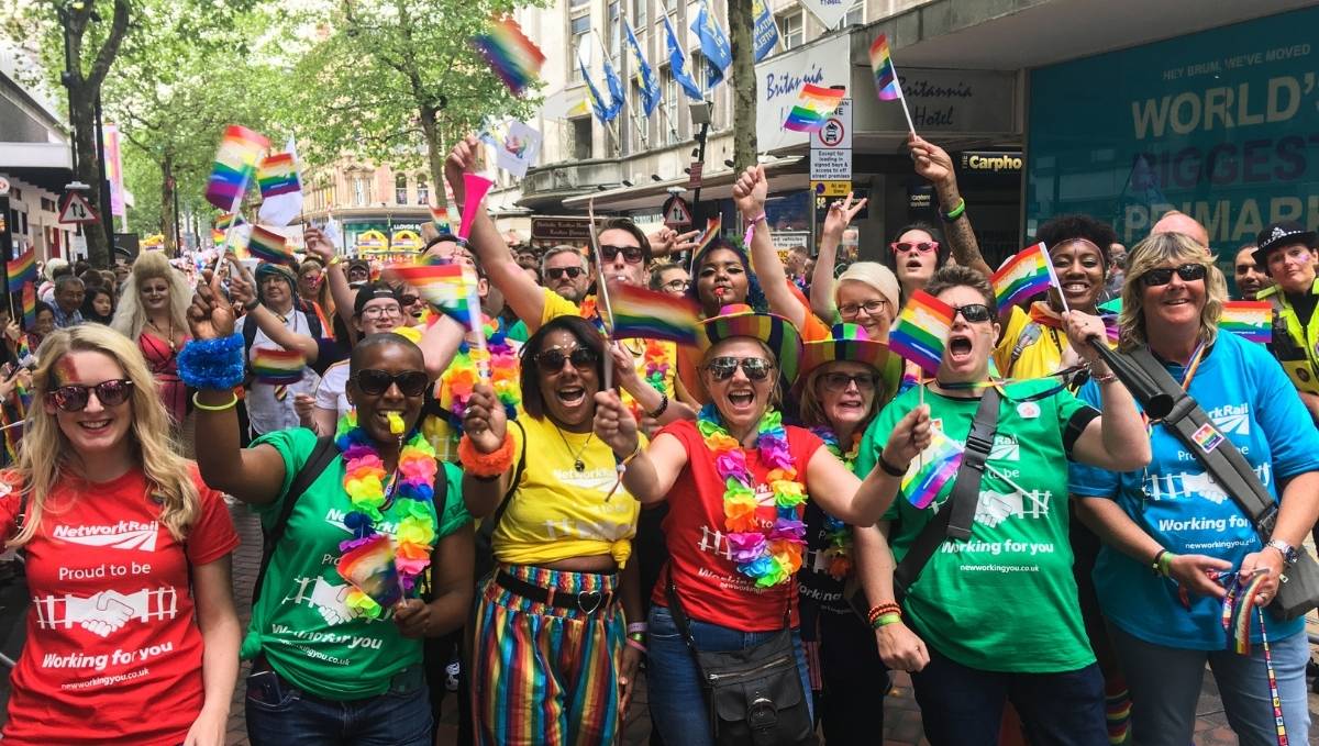 TSSA and Network Rail members in red, yellow, green and blue t-shirts at a pride rally. They are wacing rainbow flags and wearing rainbow garlands.