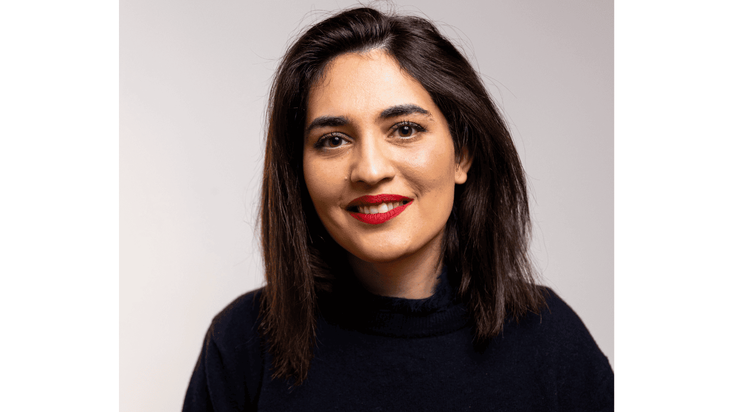 A head and shoulders shot of Maryam Eslamdoust, an Iranian woman, with long dark hair, a black top and bright red lipstick. She is smiling directly at the camera. The background is neutral.