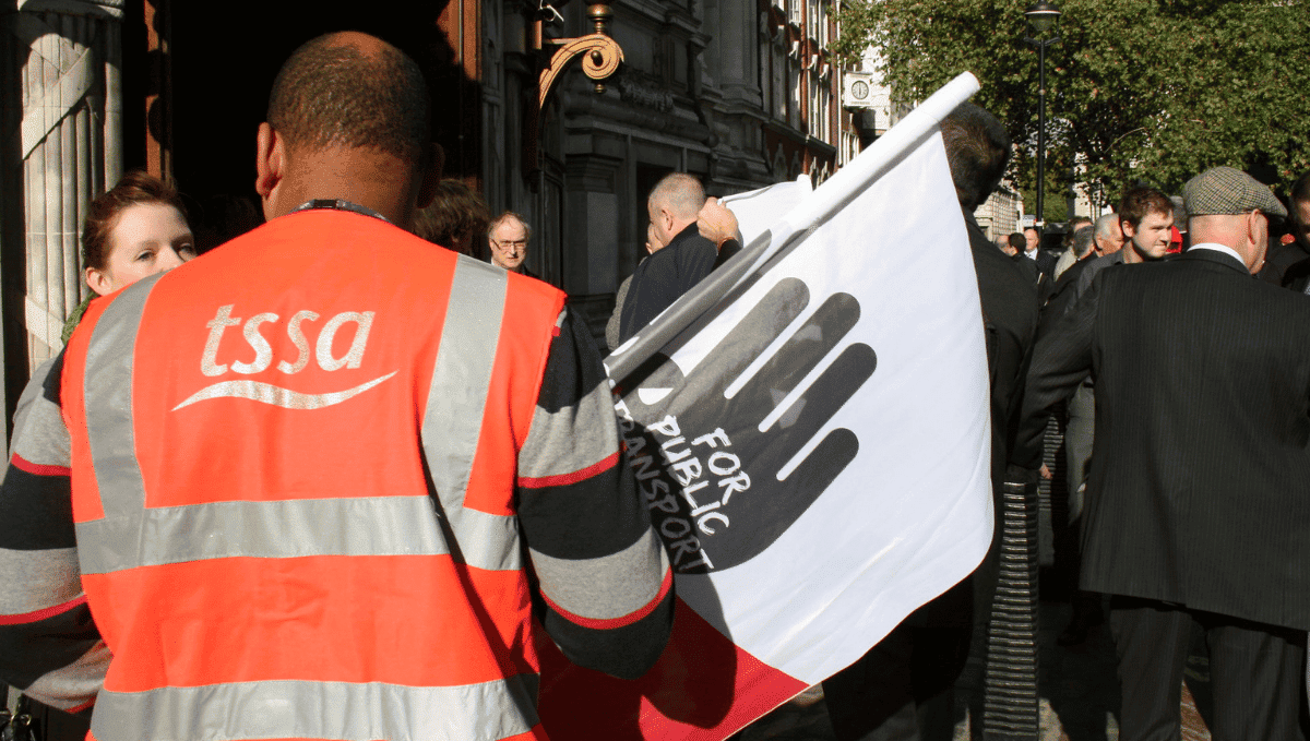 Person wearing a high vis TSSA jacket and holding a campaign flag