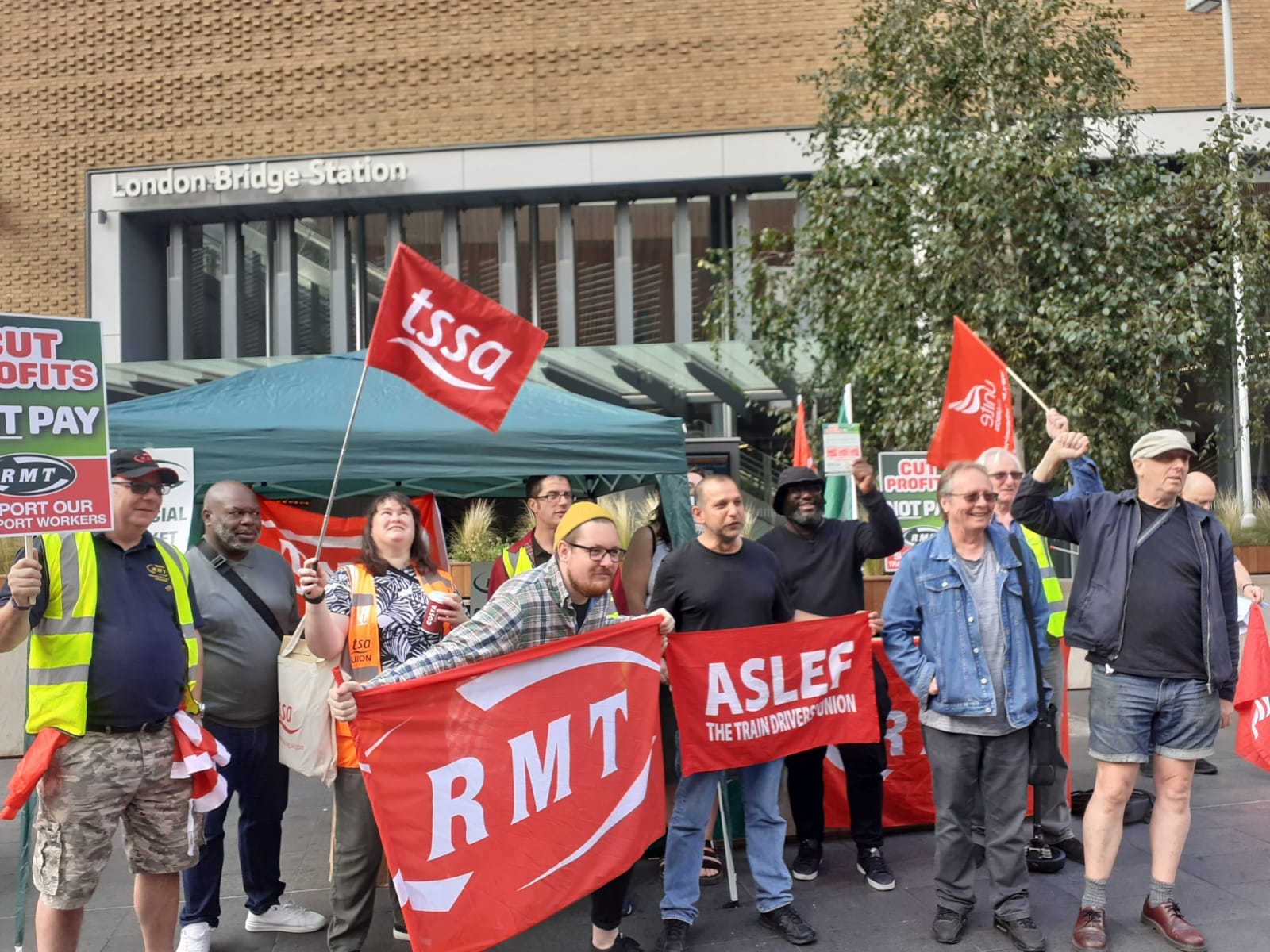 Picket Line with ten men and women holding flags from TSSA, RMT and ASLEF unions
