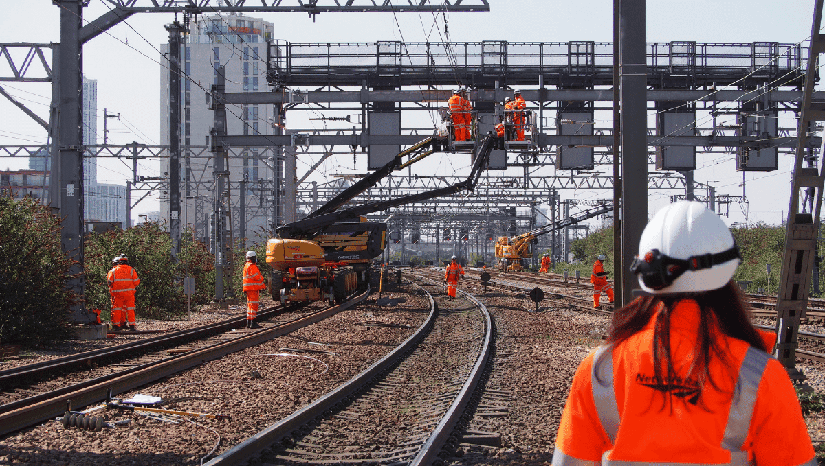 Network Rail workers in orange high vis and hard hats working on tracks and overhead lines