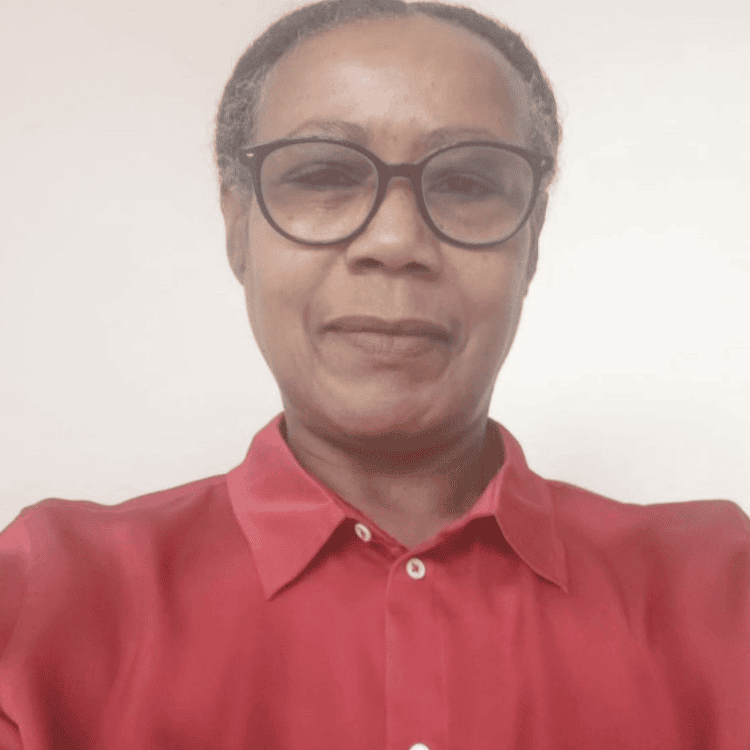 Gillian Pitter a black woman with greying hair, wearing a red shirt and glasses with black frames. She is smiling at the camera.
