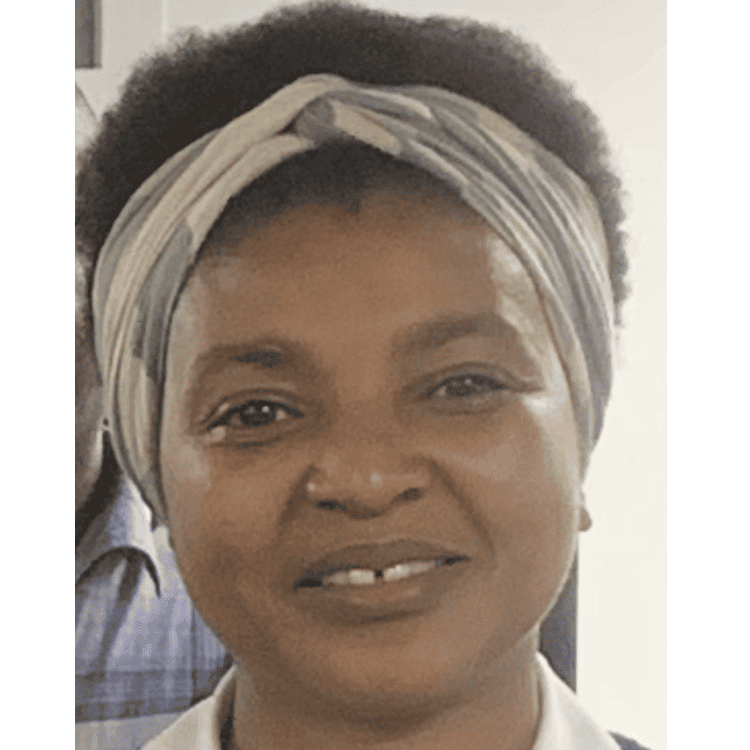 Mary Sithole, a black woman with natural hair held back with a head band. She has a gap between her two front teeth and is smiling at the camera.