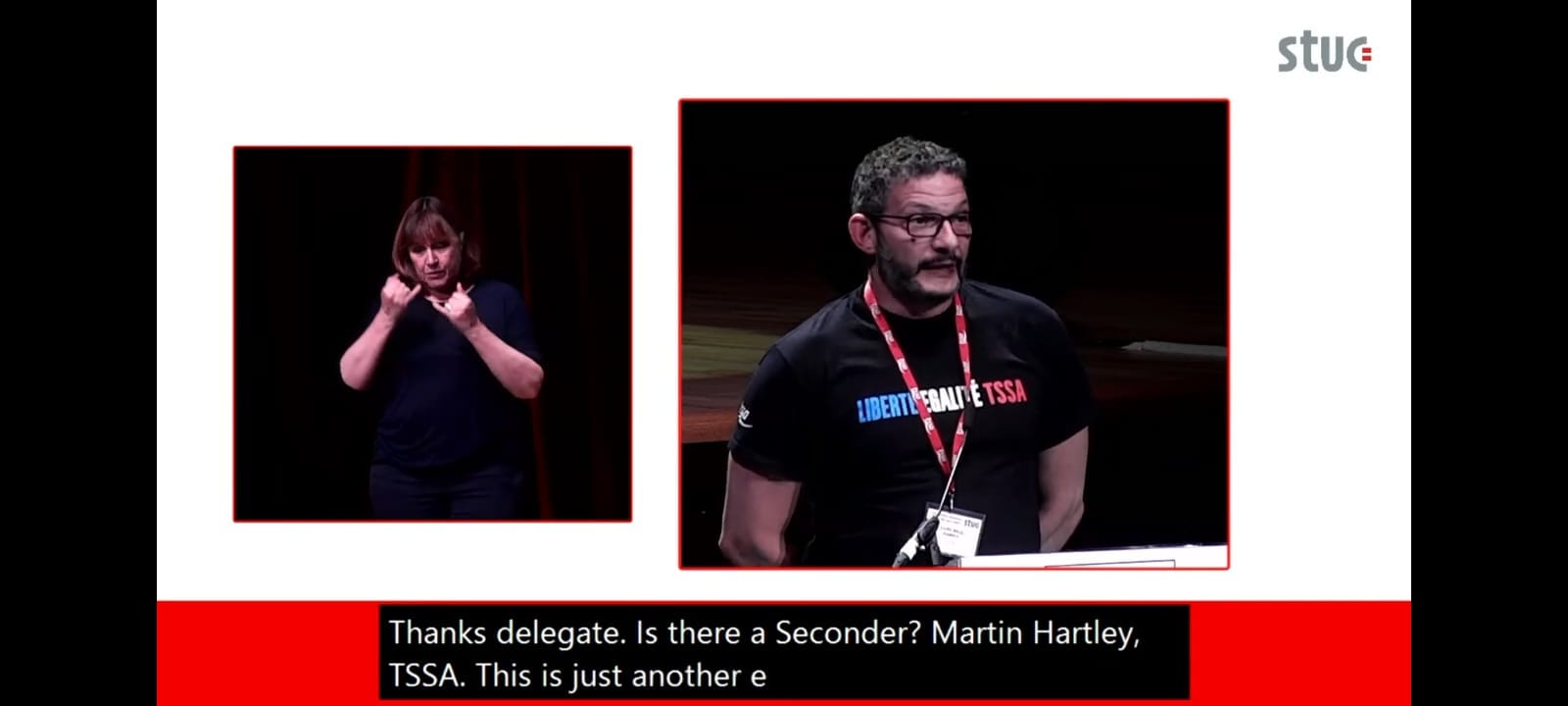 A screen showing two pictures side by side, on the left is a female sign language interpreter in a black shirt. On the right is Martin Hartley, a black man, with a moustache. He is wearing a black shirt with the words Liberté, Egalité, TSSA .