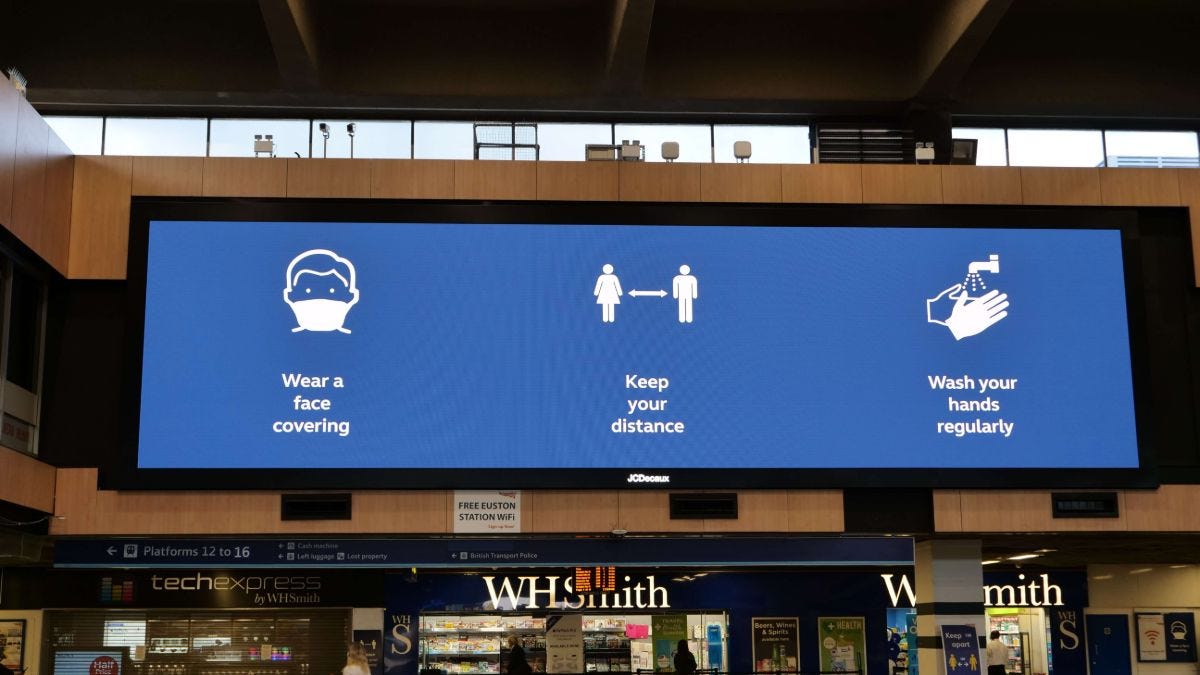 Covid advice digital sign in rail station showing hands, face, space
