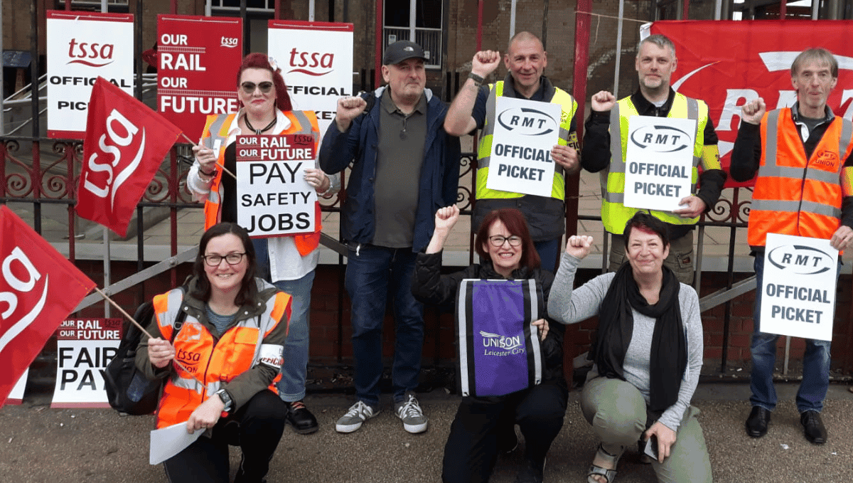 People on picket line with flags and placards at Leicester station