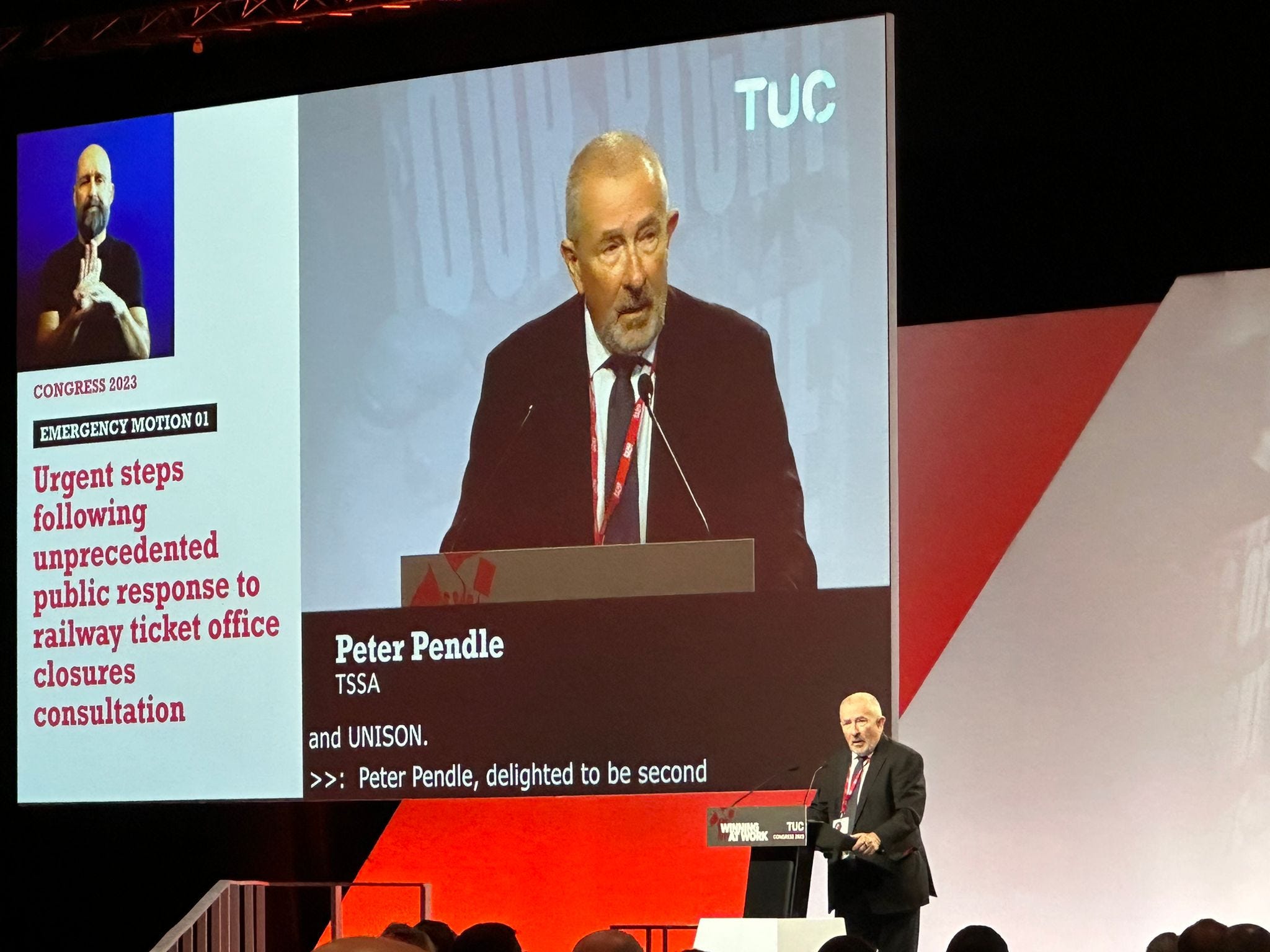 Peter Pendle, TSSA Interim General Secretary, addresses the TUC. Peter is shown standing behind a lectern in front of a larger image showing Peter and a sign language translator. 