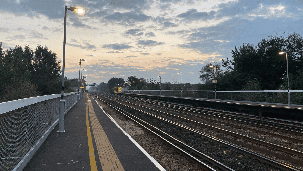 Railway tracks with platform in view and lighting on. Early morning sky.