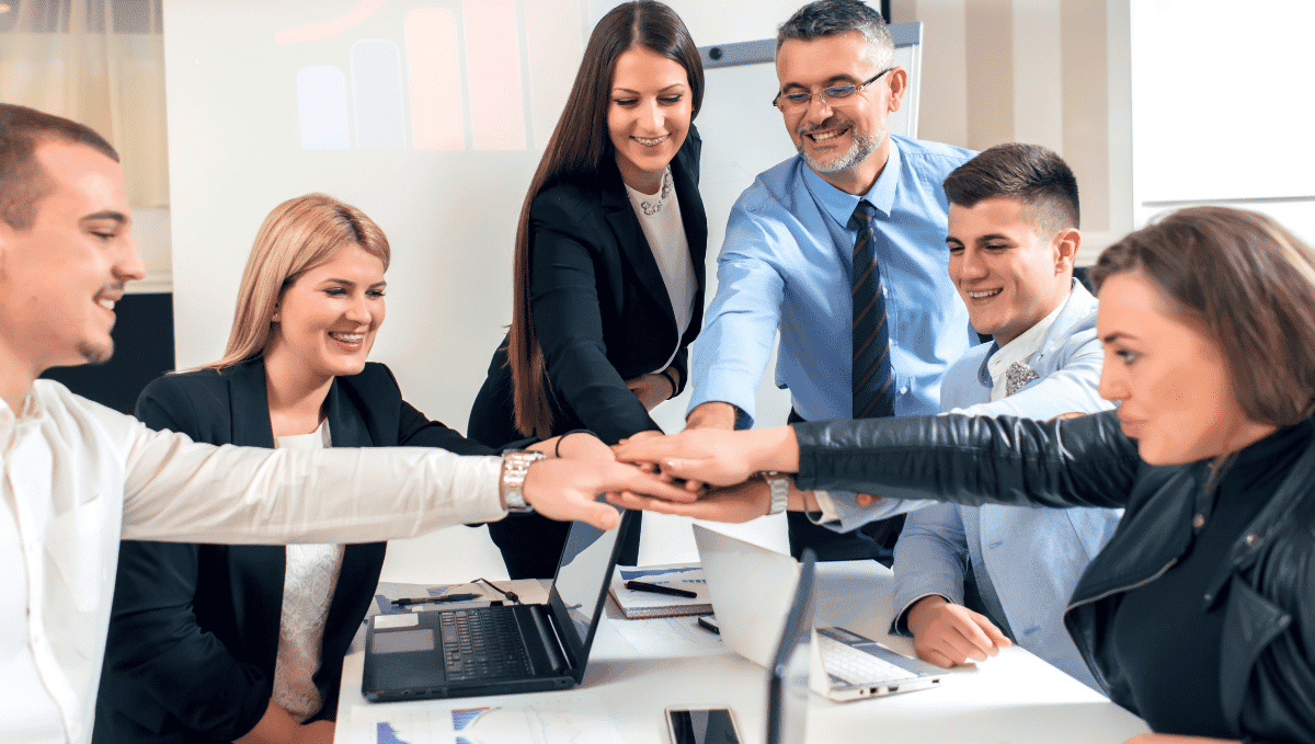 Group of office workers with hands on top of each other in the centre of the group.