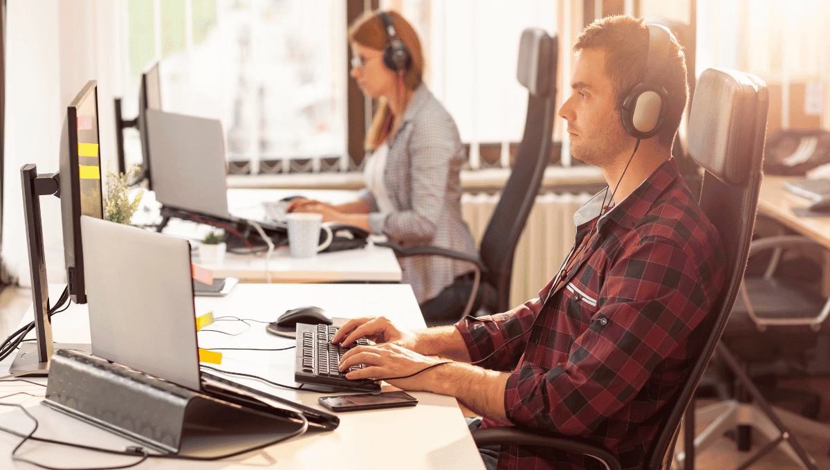 Two office workers at desks with laptops and headphones