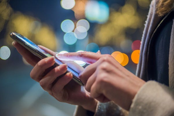 A woman's hands using a mobile phone. She has white cuffs on a coat and a French manicure.