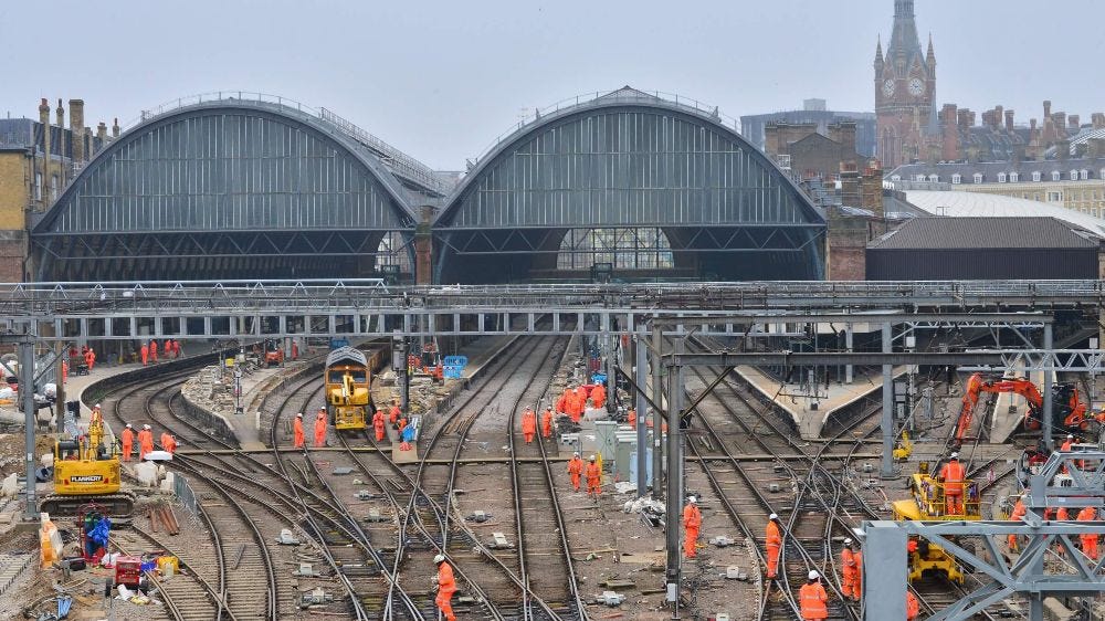 Network Rail engineers wearing high vis and helmets working on multiple tracks outside of a big station 