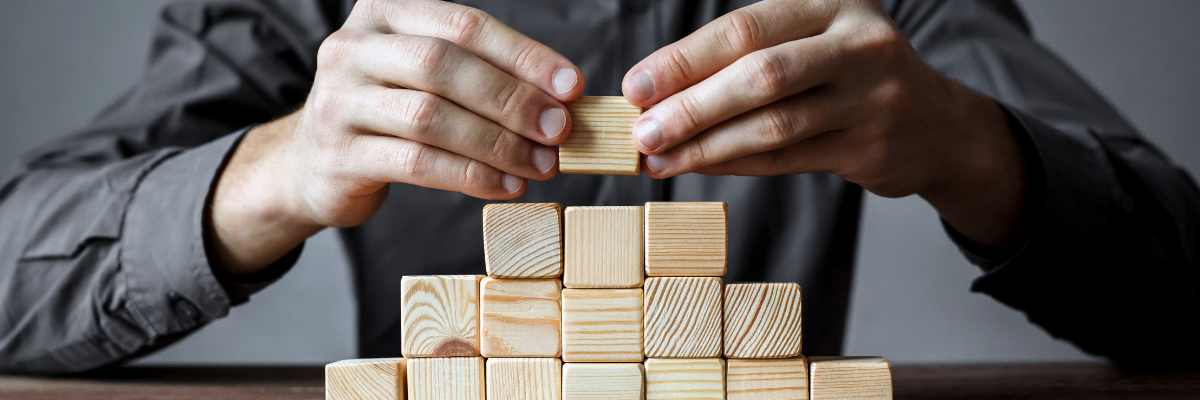 Males hands building a triangle with wooden building blocks.