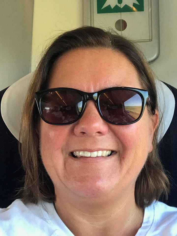 A selfie of Catherine Poole, she is wearing sun glasses and sitting on a train. 