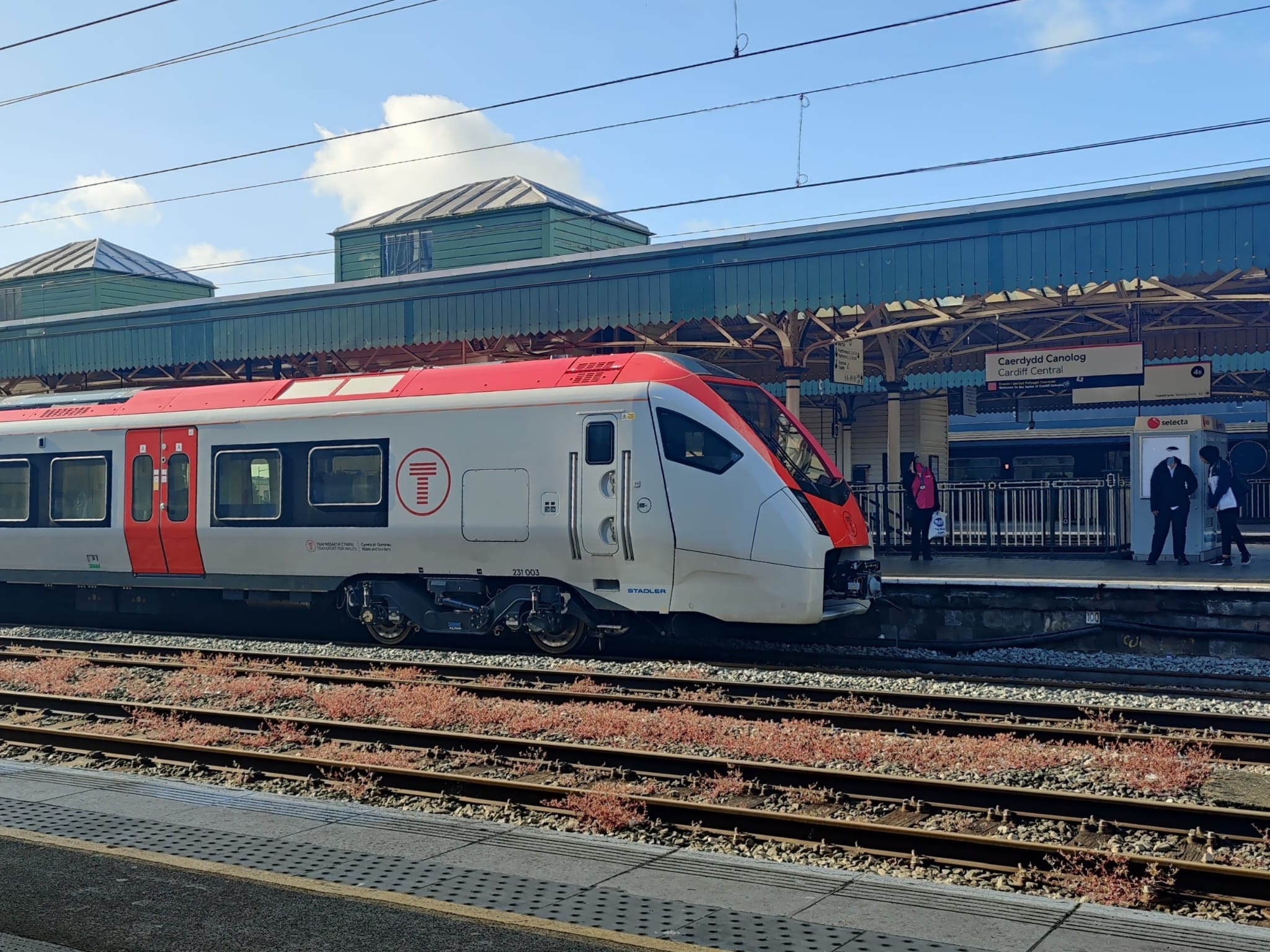 A Transport for Wales train, in white and red livery, standing at the platform in Cardiff Central station.