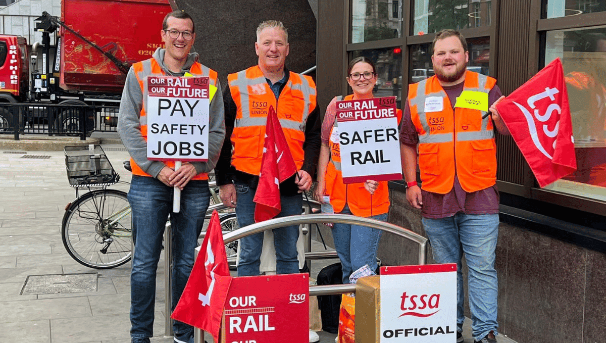 Four TSSA members on a strike picket line with flags, signs and high vis jackets