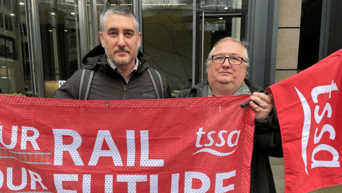 Luke Chester and Mick Carney holding TSSA flags outside Rail Delivery Group 