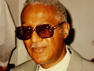 Black activist and TSSA EC member Clade James, in a suit, smiling and wearing sunglasses.