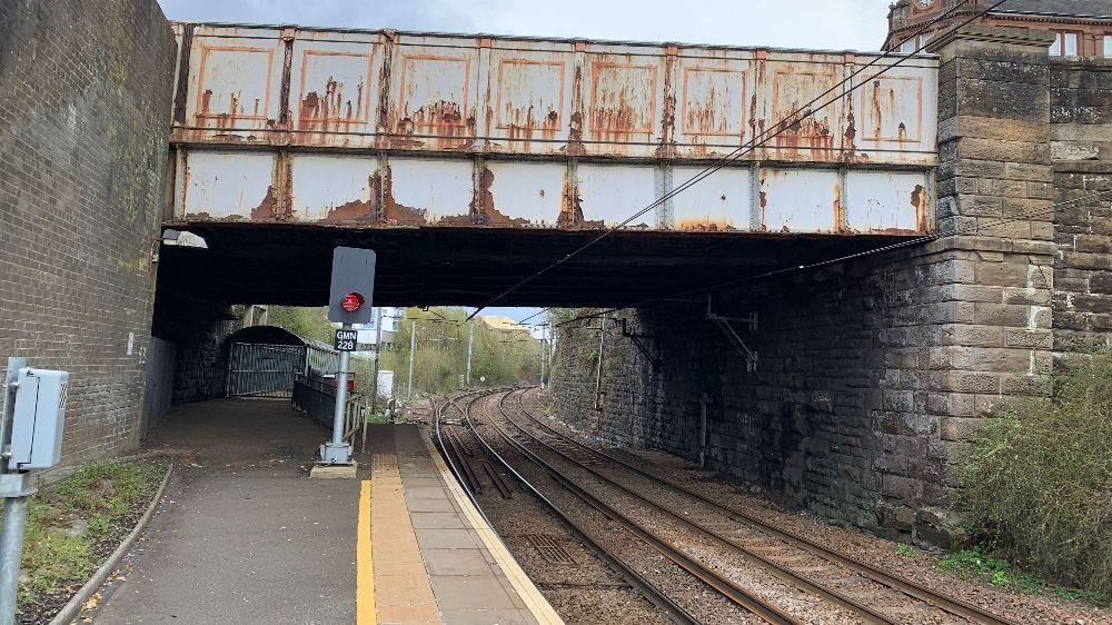 Shabby rusting bridge over railway tracks with red signal