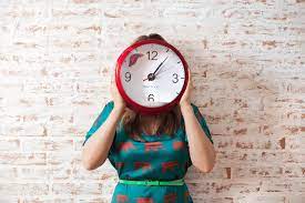 Person holding red clock in front of their face.